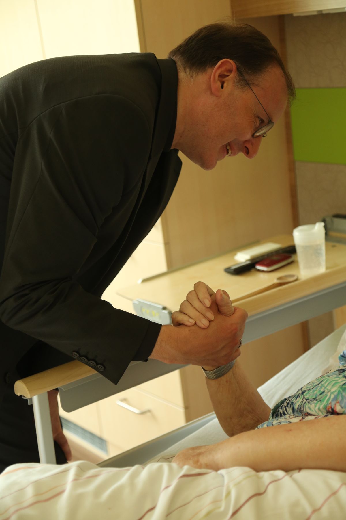 Der Weihbischof besucht eine Frau im Hospiz. Er unterhält sich mit ihr, hält ihre Hand und sie spenden sich gegenseitig den Segen.