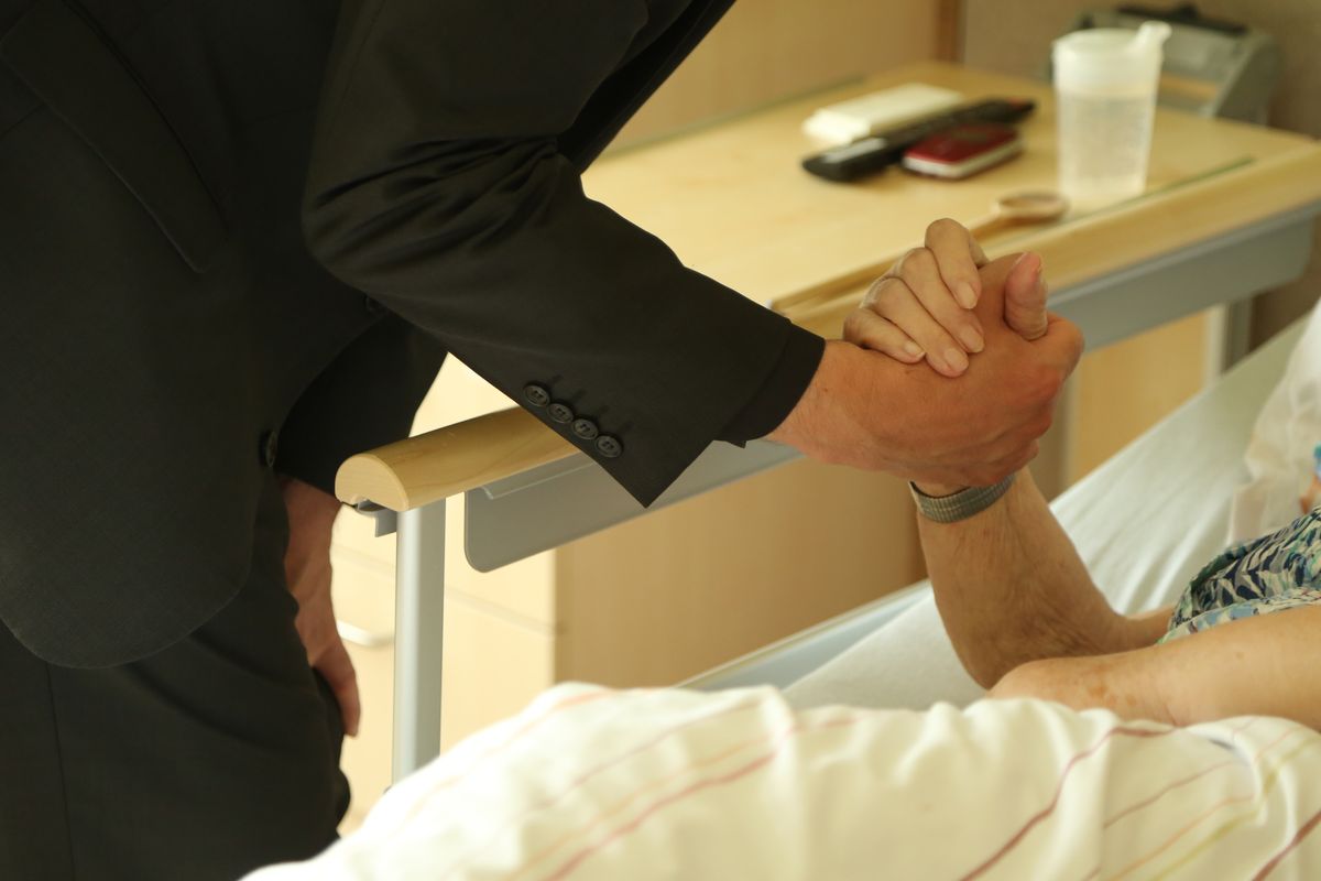 Der Weihbischof besucht eine Frau im Hospiz. Er unterhält sich mit ihr, hält ihre Hand und sie spenden sich gegenseitig den Segen. 