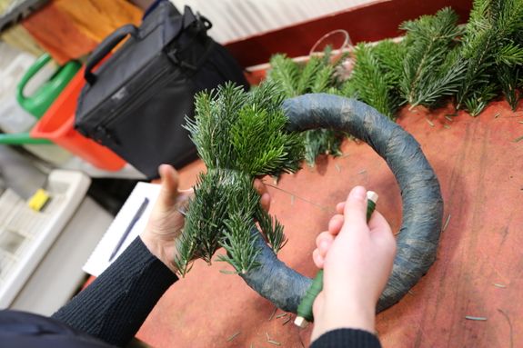 Im Anschluss wird eine neue Schicht Grün auf die vorherige Schicht gelegt. Die Zweige sollten sich immer überlappen. Diese Technik wird wiederholt, bis der ganze Kranz einmal umwickelt wurde. Wichtig ist es, den gesamten Kranz einmal zu umrunden.