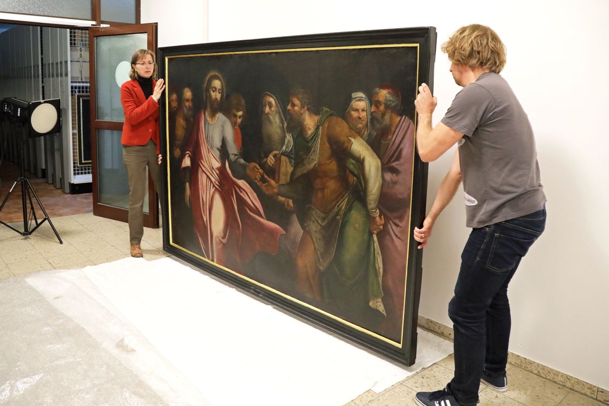 Für den Transport in die Werkstatt muss das Bild zunächst aus dem Rahmen gelöst werden. Restauratorin Gudrun Hanika und Christoph Deuter, wissenschaftlicher Mitarbeiter des Kunstreferats, machen sich bereit, um das Gemälde vorsichtig auf den Boden zu legen. 